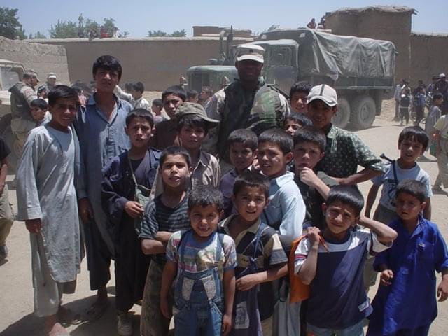 A man in U.S. military uniform stands amongst a group of Afghani children